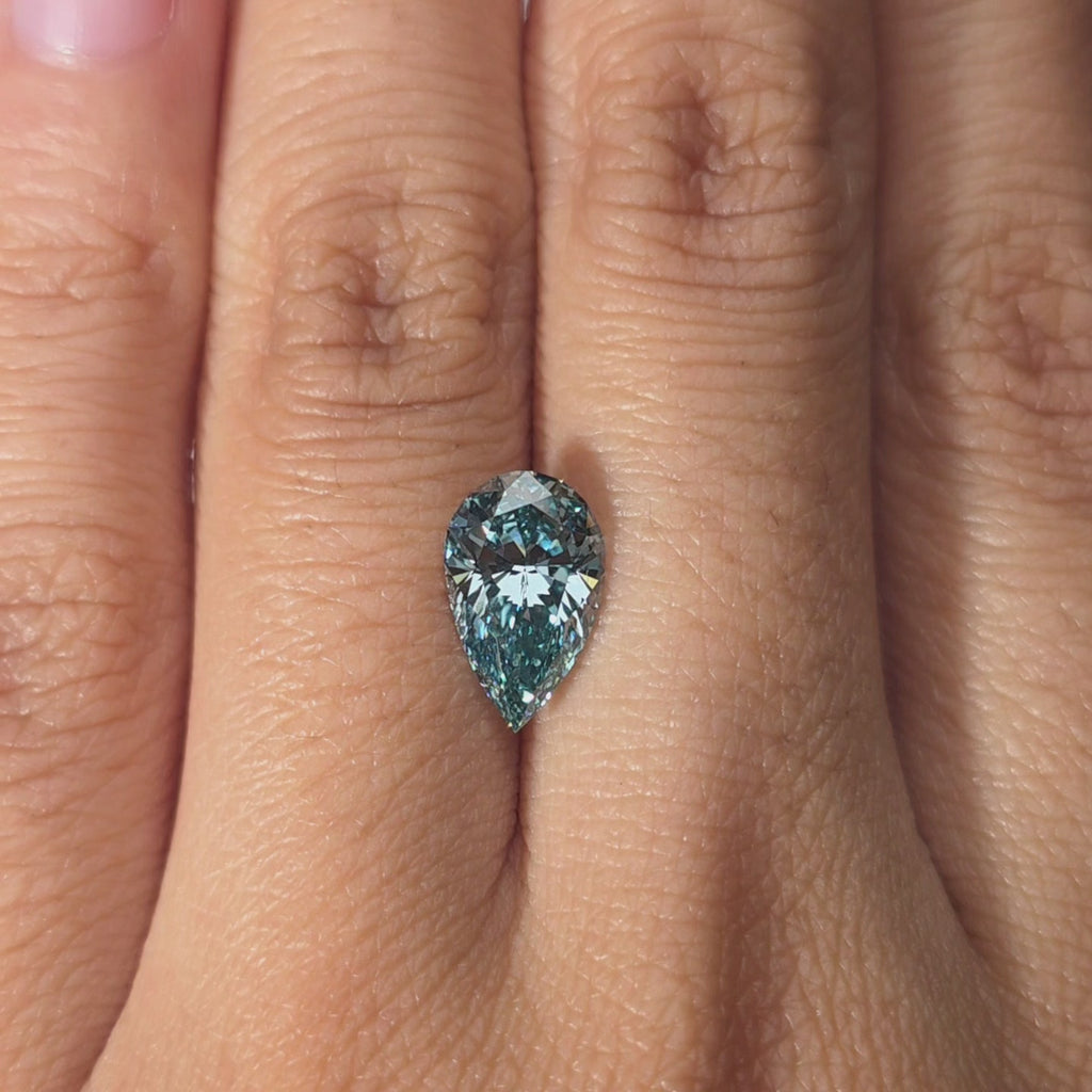 Hand modeling a 2.05ct pear cut fancy vivid blue lab diamond in warm indoor light.