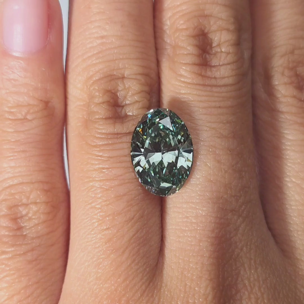 Hand modeling a 5.00ct oval cut fancy deep green VS1 lab diamond in warm indoor light.