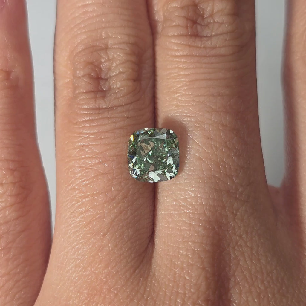 Hand modeling a 2.131ct cushion cut fancy vivid green VS1 lab diamond in warm indoor light.